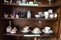 Two shelves filled with various small china and porcelain items including teacups, dessert plates, perfume bottles, figurines and vases