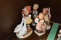Front view of four Goebel figurines showing girl with swans, girl with basket and letter, and two other children.