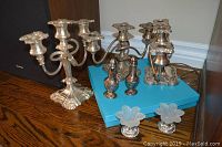 Two silver plated candelabras, salt and pepper shakers, and serving platter displayed on a wooden surface with blue box background, showing tarnished condition and need for polishing.