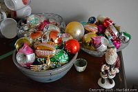 View of hand-thrown pottery bowls filled with colorful vintage glass Christmas ornaments, along with crystal bowl and Santa figurine on tabletop.