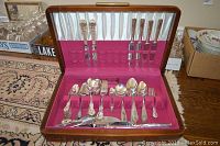 Complete view of the open wooden case showing two sets of silver plated cutlery on pink and white fabric lining.