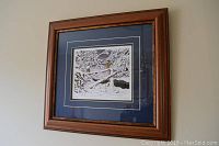 Photo of framed print showing snow-covered winter scene with trees and stream.
