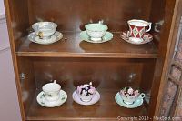 Six teacup and saucer sets displayed in cabinet