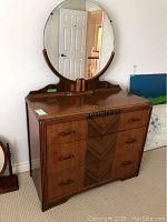 Front view of the vintage wooden dresser with oval mirror attached, showing drawer layout and decorative wood grain.