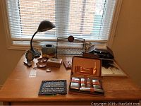 Photo showing the entire lot arranged on a wooden table by the window, includes study lamp, music boxes, mini bench, shaving kit, framed photos, and assorted smaller decorative items.