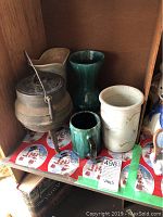 View of pottery vases and green mug alongside cast iron kettle with lid and handle.