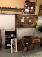 View of the pegboard with vintage tools, wooden boxes on the floor including the yellow Keens mustard box, and shelving unit.