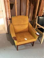 Front angled view of teak frame armchair with yellow fabric upholstery showing wear and tear.