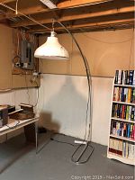 Full view of arc floor lamp standing against basement wall next to bookshelf