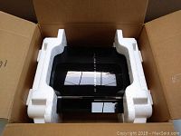 Open cardboard box with black PlayStation 3 console secured in white styrofoam supports inside.