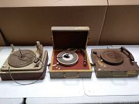 Photo of three vintage portable turntables in cases, showing the devices side by side on a table.