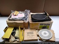 Photo showing the Garrard SP20B turntable on its box alongside another boxed turntable with additional accessories and manuals laid out around it.