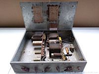 Top open view of vintage tube amplifier showing internal vacuum tubes, transformers, capacitors, and wiring with rusted metal chassis.