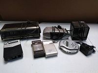 Photo of a collection of vintage electronic devices tied together including a flip clock, portable radio, cassette players, CD player, and power adapter on a white surface.