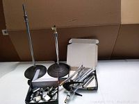 Overview of the lot showing two black microphone stands with round bases, a box of metal clips, and a box of metal rods and attachments.