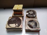 Top view of the lot showing stacks of vintage recording tape boxes with two reels, one metal spool and one clear plastic spool, resting on top.