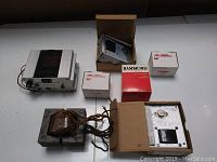 Top down photo showing multiple vintage transformers and power supply with some in original Hammond boxes on flat surface.