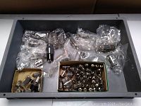 Top view of a large gray container filled with numerous vintage vacuum tubes, some packed in plastic bags, some loose in boxes.