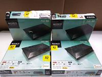 Four Sony BDP-BX110 Blu-ray Disc/DVD players in original boxes showing front and top of packaging with regional R2 stickers and Sony branding