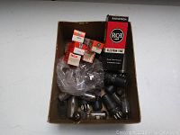 Box containing mixed vintage electron tubes with some in original packaging and several loose tubes.