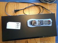 Top view of the black Samsung Blu-ray player with power cord and remote on top of it.