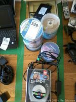 Top-down view showing spindles of writable DVDs, several writable CDs, Memorex mini DVD-R pack, and LG DVD writer unit with USB cable.