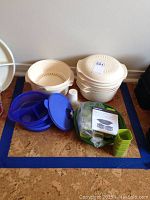 Beige Tupperware steamer baskets stacked with vented lids, blue containers with lids, green measuring cups and an instruction manual packed together.