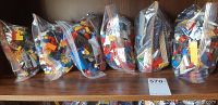 Six clear plastic bags filled with assorted LEGO pieces in various colors and sizes on a wooden shelf.