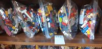 Six transparent resealable bags filled with assorted LEGO pieces in multiple colors and forms, placed lined up on a wooden surface.