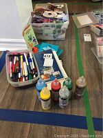 Wide view of craft supplies including embroidery paints, pens, storage containers, and stencil books.