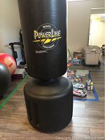 Full view of the black PowerLine training bag with weighted base filled with water or sand, standing upright on floor indoors.