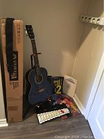 Wide shot showing the blue J. Reynolds 3/4 acoustic guitar on a stand along with a Yamaha box, a 20-note bell chromatic xylophone, and several music books including Beatles and Led Zeppelin collections.