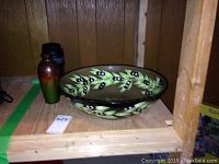 Large olive-branch patterned ceramic bowl, small gradient-colored vase, and two small thermoses on wooden shelf
