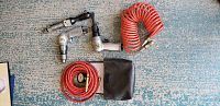 Top view showing five Sioux air tools including drill, ratchet wrench, and hammer with red coiled air hose and black pouch on floor with blue carpet.