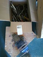 Mastercraft bench vise mounted on wood block shown inside a cardboard box with tools.