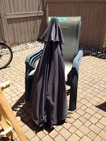 Two patio chairs side by side with closed outdoor umbrella positioned between, showing umbrella fabric condition and chair detail.
