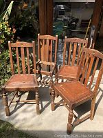 Four vintage solid wood chairs arranged outdoors showing overall condition and style