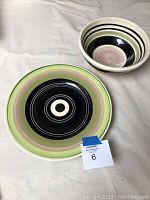Matching ceramic serving bowl and plate arranged on white fabric surface, clearly showing striped patterns and colors.