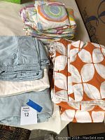 Blue, orange and multicolored patterned folded bedding sets displayed on bed including sheets, pillowcases, and duvet covers.