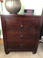 Front view of one dark wood three-drawer night table with metal handles, showing its polished finish and solid wood construction.