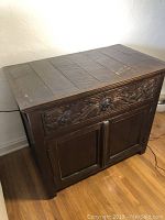 Full front view of the dark wood Indonesian side table/cabinet with closed drawer and cabinet doors, showing the carved drawer front and wood paneling.