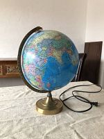 Light up globe with detailed world map, brass-colored metal base, and power cord visible on a table.