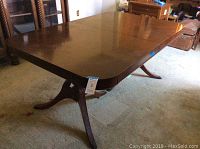 Side view of rectangular mahogany dining table with curved legs and metal casters, showing side profile and part of the leaf extension.