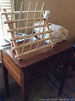 Wooden sewing table with thread holder rack, spool of white thread, fabric and patterns in natural light near window