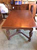 Wooden dining table showing full tabletop with carved legs and ends with leaf sections pulled out.