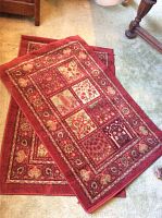 Two red floral and geometric pattern rugs, folded and stacked, showing detailed design and color.