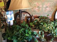 Photo showing faux plants, copper pitcher, clock, lamp base and shade, tissue holder, and dragonfly art in background.
