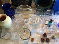 Top view showing assorted glass and ceramic vases, small glass jars, and brown candle holders on a white surface.