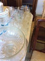 Multiple clear glass cups and glasses of various sizes including handled cups next to the punch bowl