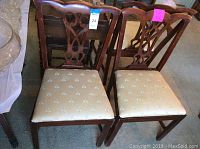 Front view of two wooden dining side chairs with carved backs and beige bee print fabric seats, showing overall condition including wood wear and fabric stains.